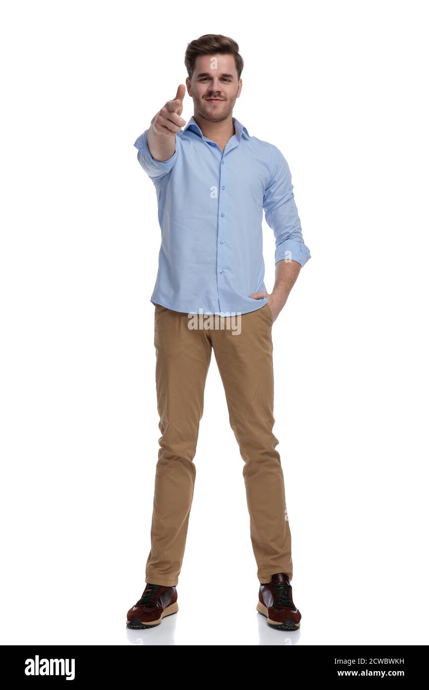 Positive casual man holding finger gun and hand in pocket while wearing shirt and standing on white studio background Stock Photo