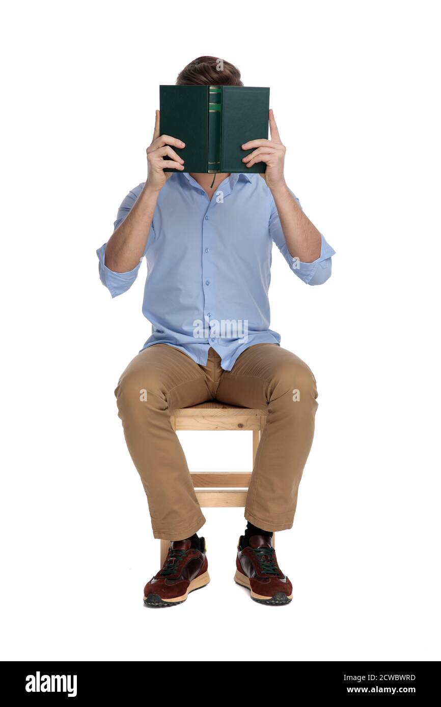 Young casual man covering his face with a book while sitting on a chair ...