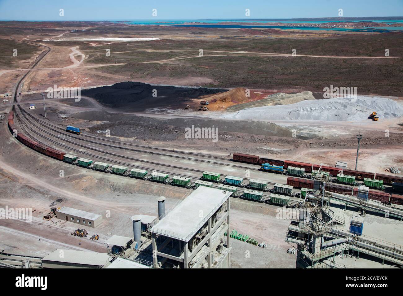 Mynaral/Kazakhstan, Jambyl Cement plant. Cargo train terminal and heap of clinker minerals. Balkhash lake on horizon. Stock Photo