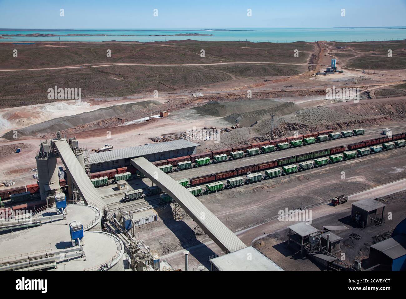 Mynaral/Kazakhstan - April 23 2012: Jambyl Cement plant. Hopper car train terminal. Conveyor and heap of clinker minerals. Balkhash lake on horizon. Stock Photo