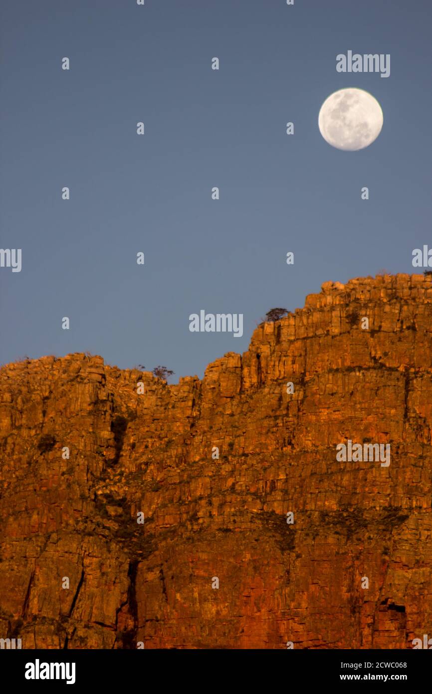 The full moon rising over a reddish colored, sandstone cliff of the Cederberg Mountains, South Africa, Stock Photo