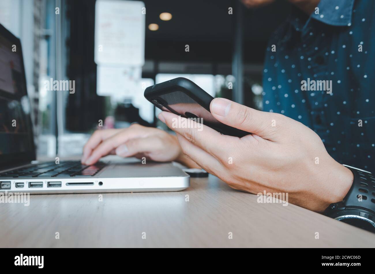 business man holding a cell phone looking at work data and laptop computers on the desk at the office.business and technology concept Stock Photo