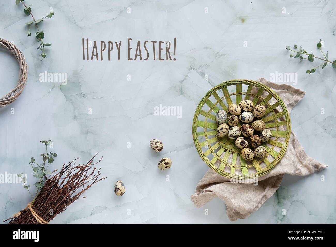 Quail Easter eggs, natural Spring decorations and eucalyptus twigs. Flat lay on marble table, text Happy Easter. Stock Photo