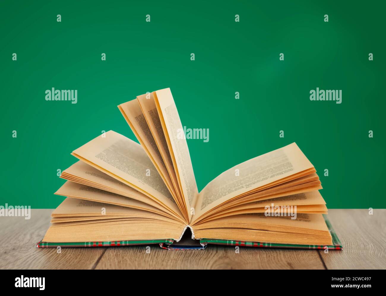 Open book textbook in colorful cover on a green background. Back to school distance home education.Quarantine concept of stay home Stock Photo