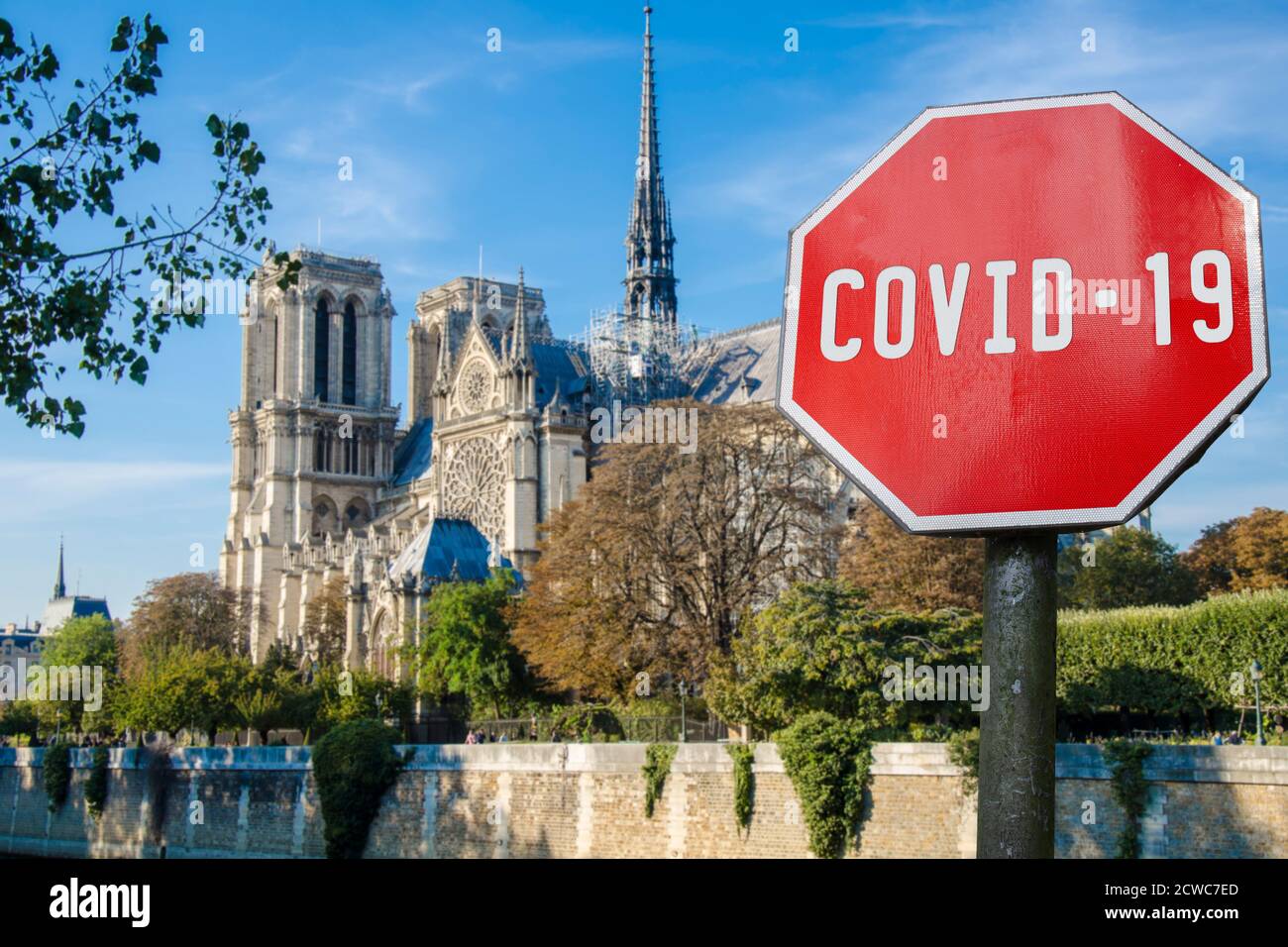 COVID-19 sign against view of Notre Dame de Paris or Notre-Dame Cathedral in Paris Stock Photo