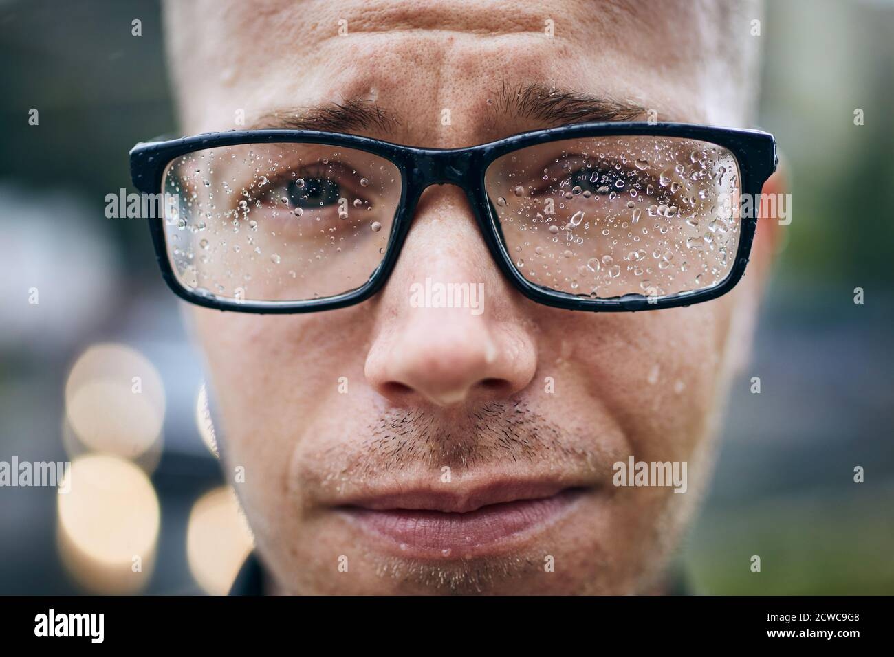 Portrait of young man with eyeglasses in rain. Selective focus on raindrops. Stock Photo