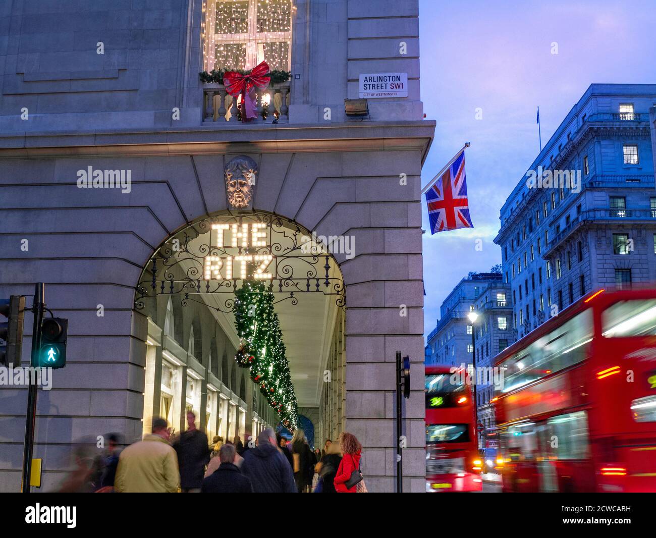 The Ritz Hotel at Christmas festive season, evening night lights ‘The Ritz’ sign illuminated, with a Union Jack flag, shoppers and passing London red buses Arlington Street Piccadilly London UK Stock Photo