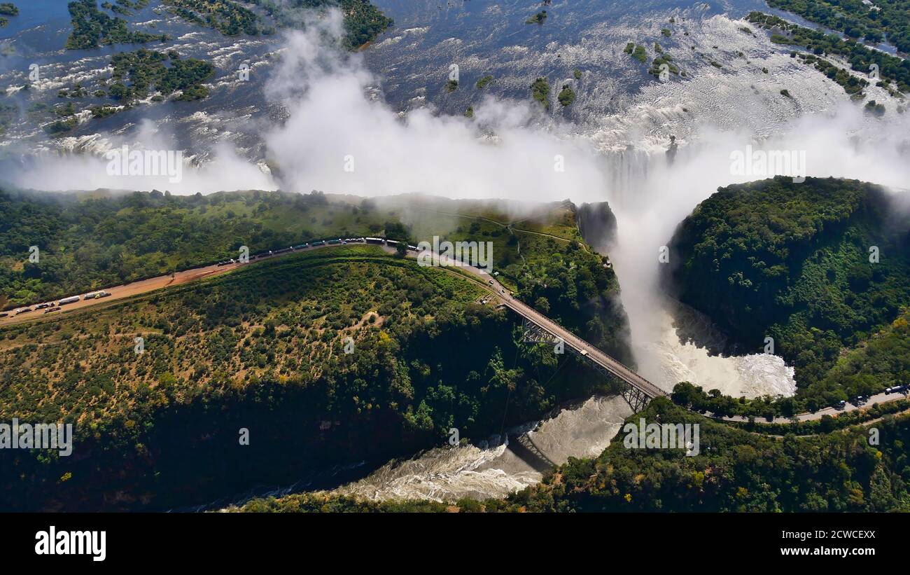 Stunning aerial panorama view of the majestic and powerful Victoria Falls (largest waterfall worldwide) with historic bridge. Stock Photo