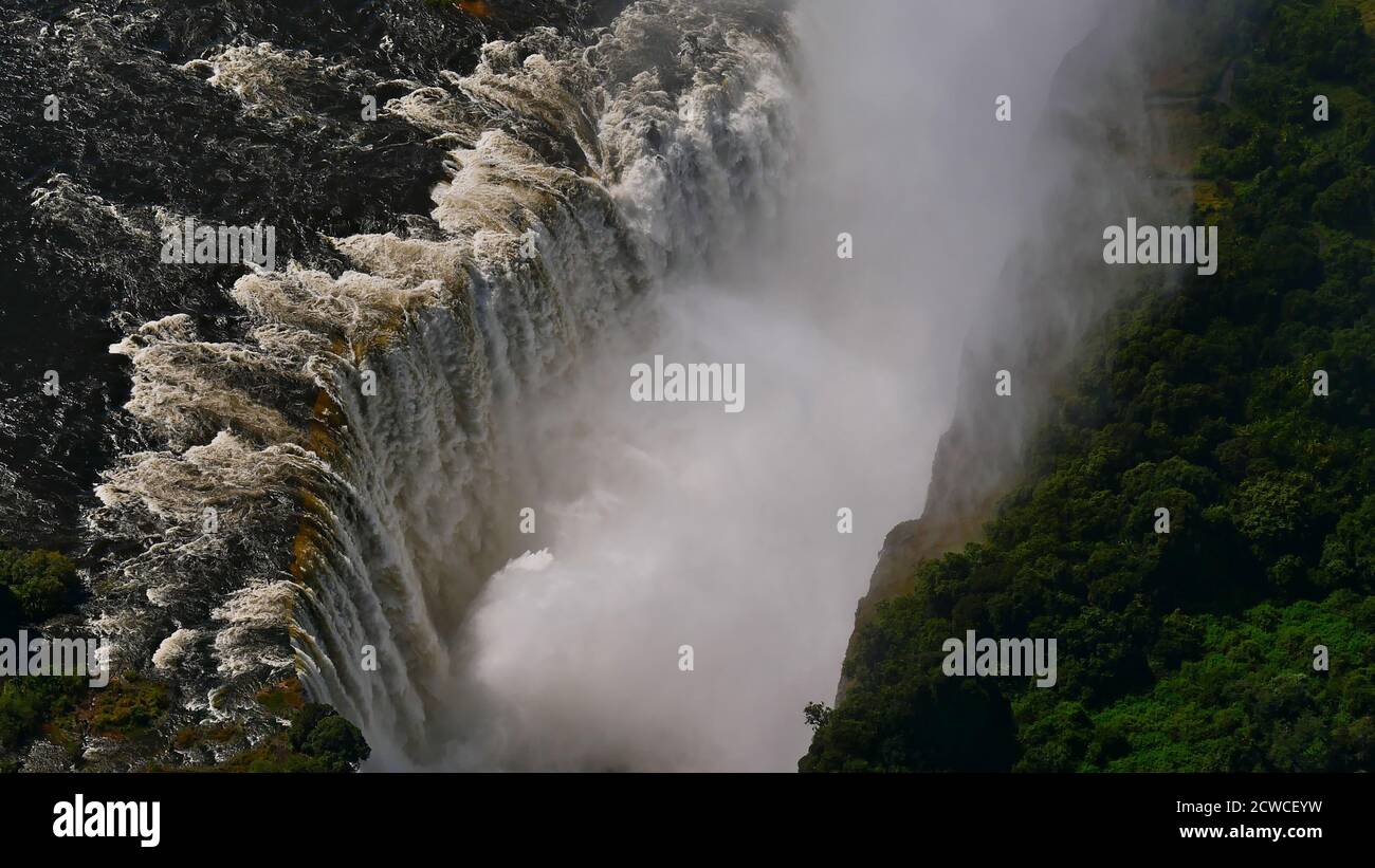 Closeup aerial view in abysm of majestic Victoria Falls and rainforest with enormous water spray at the end of rainy season from helicopter. Stock Photo