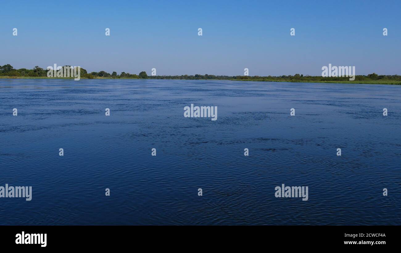 Wide view over peacefully flowing Okavango river with riverbanks from safari boat near Divundu, Caprivi Strip, Bwabwata National Park, Namibia, Africa Stock Photo