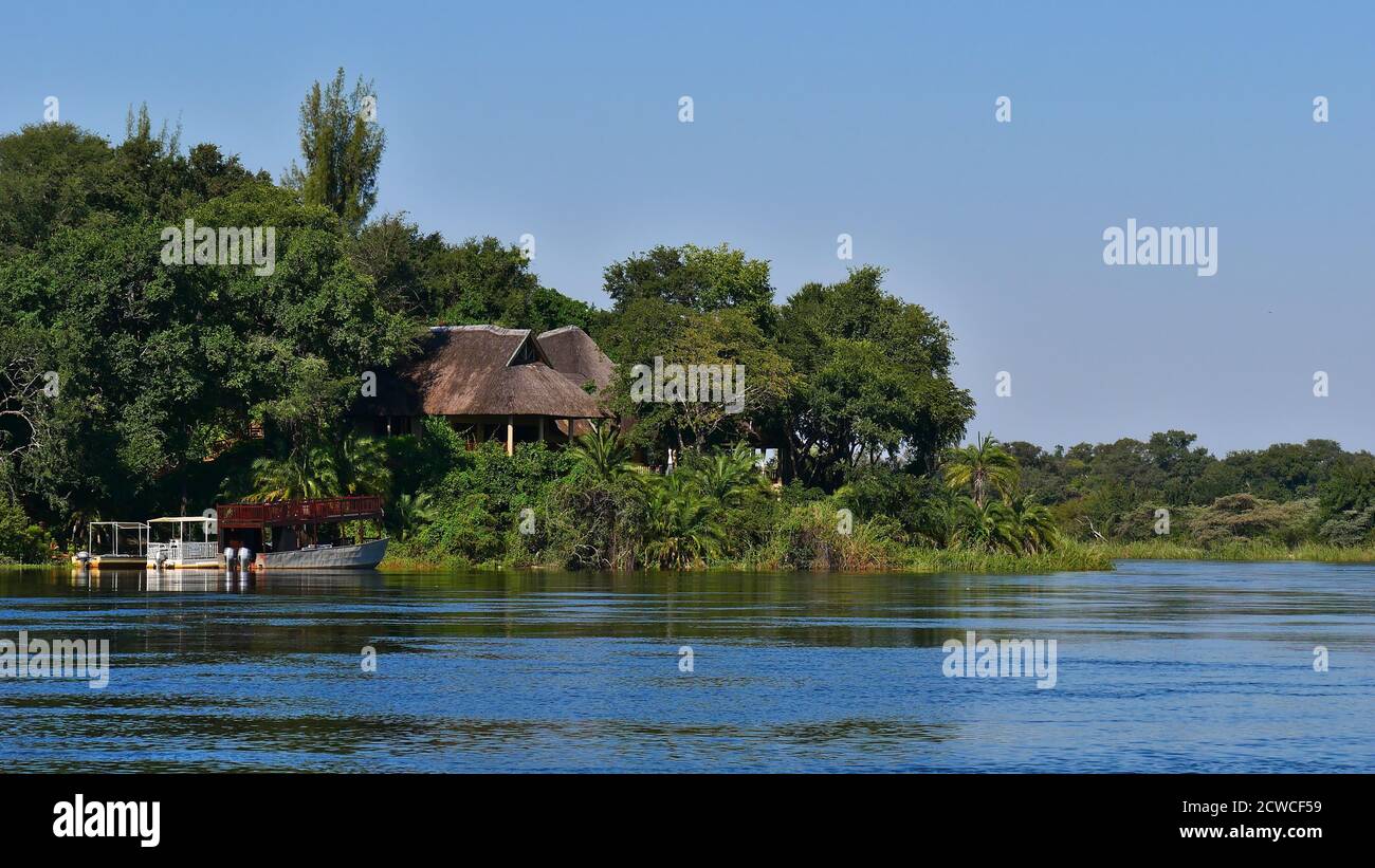 Bwabwata National Park, Botswana - 04/27/2018: Safari lodge at the riverbank of Okavango River surrounded by dense vegetation with docking boats. Stock Photo