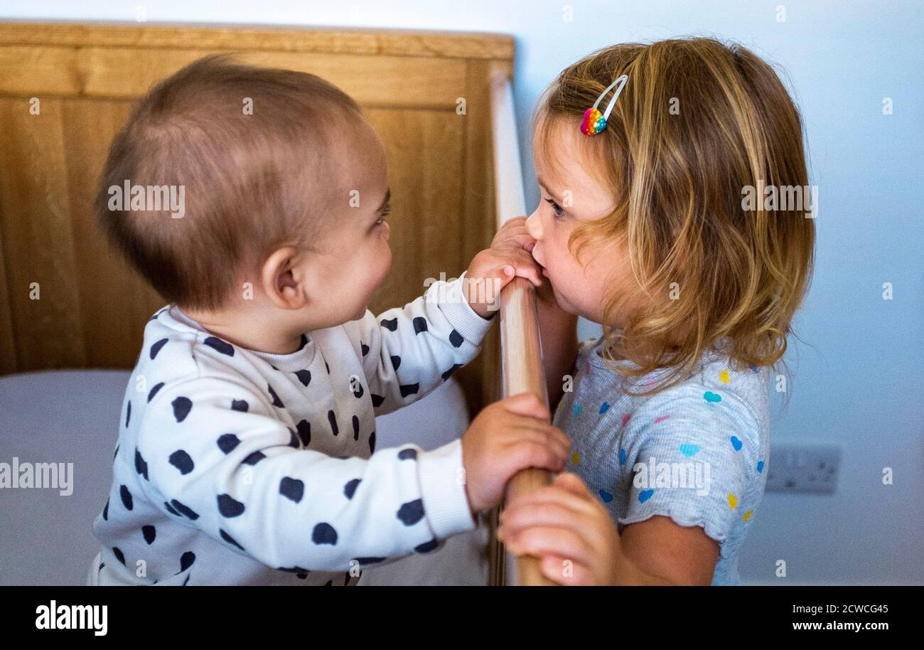 3 year old girl with little baby brother of 10 months playing by his cot - lifestyle family everyday life Stock Photo