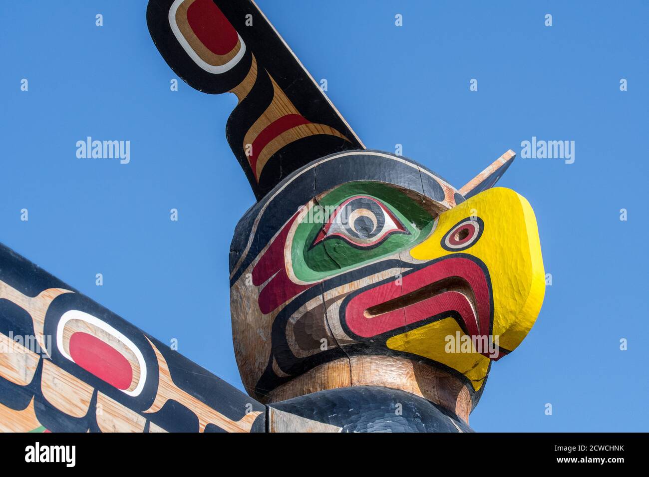 Colourful wooden carved Canadian totem pole showing eagle's head against blue sky Stock Photo