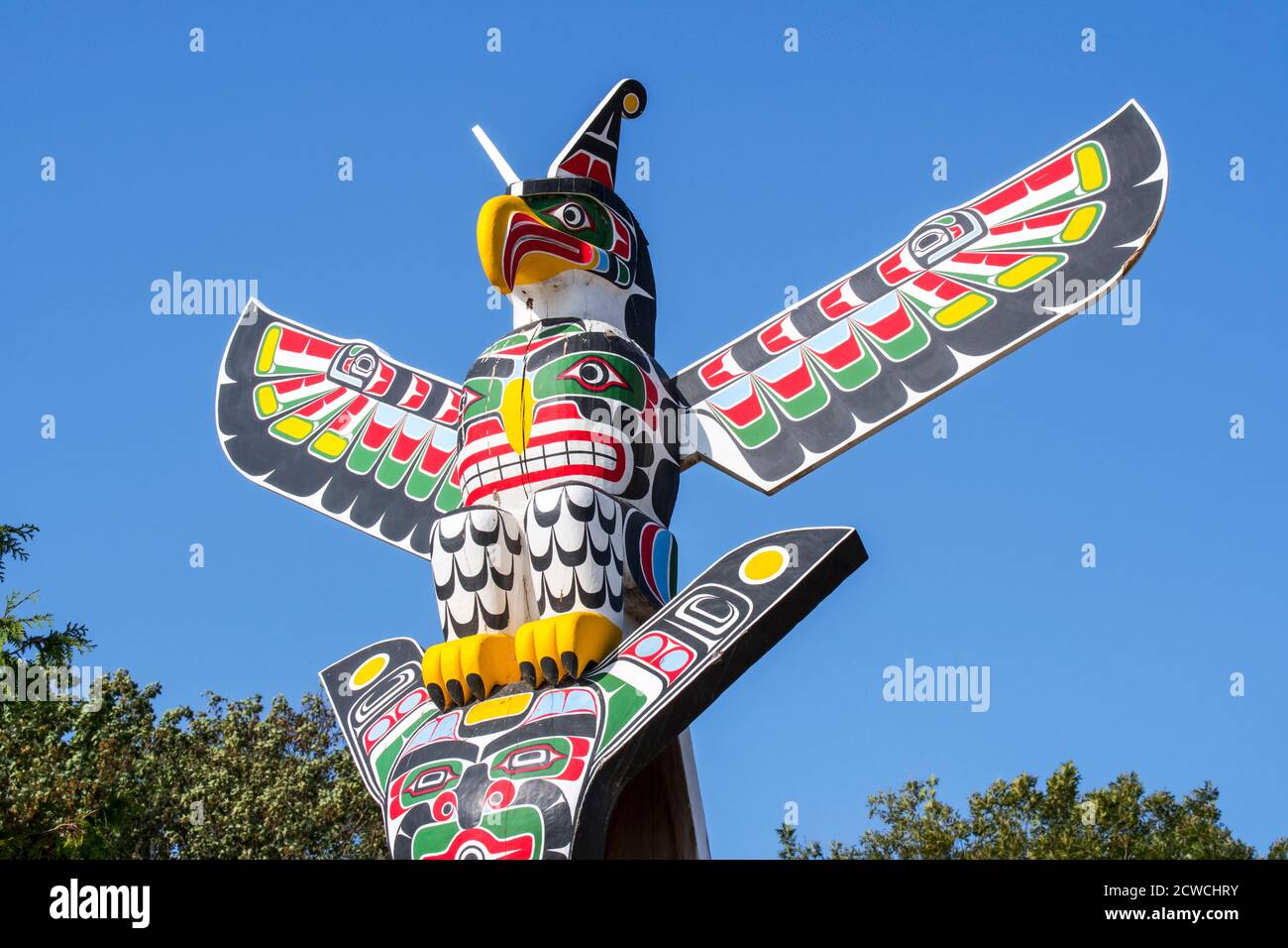 Colourful wooden carved Canadian totem pole showing eagle against blue sky Stock Photo