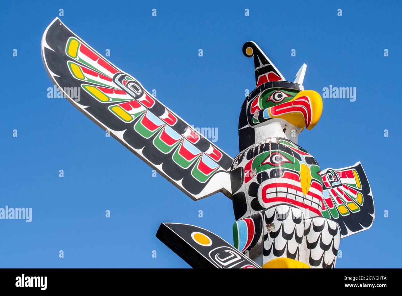 Colourful wooden carved Canadian totem pole showing eagle against blue sky Stock Photo