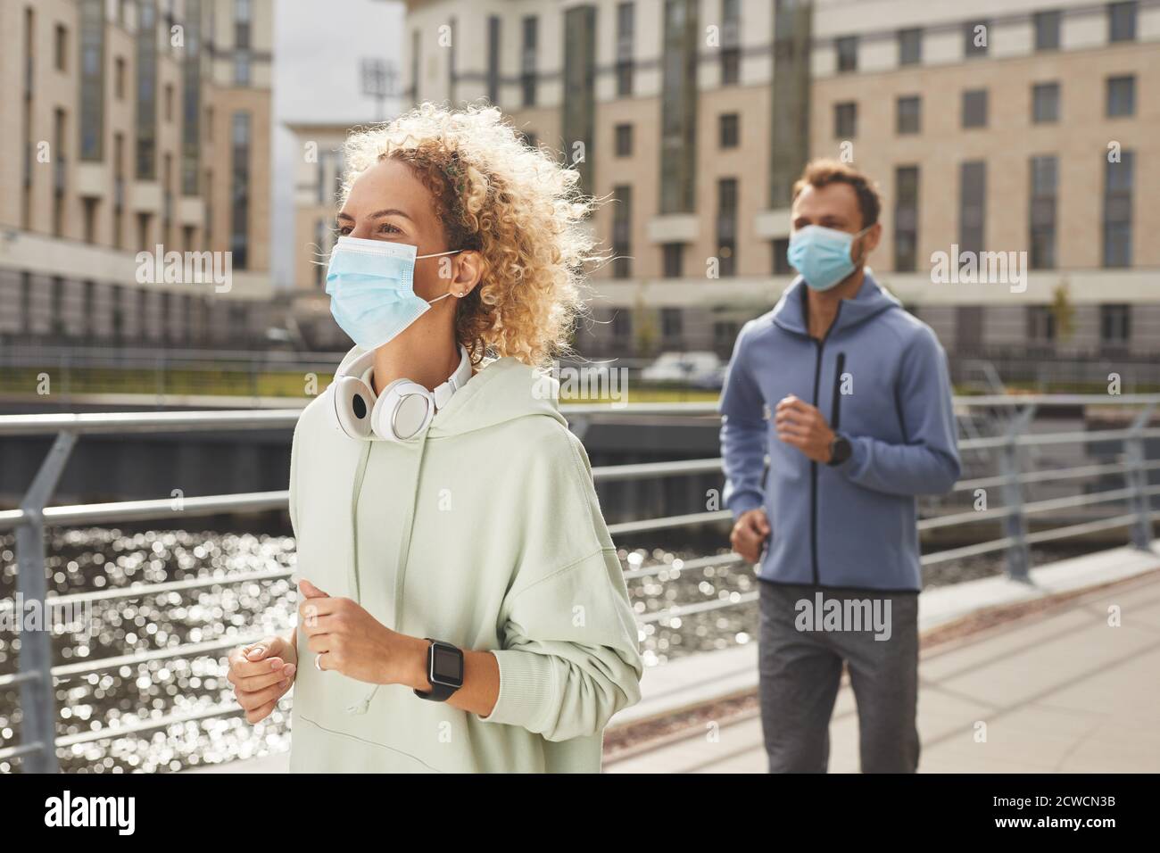 Young couple in sports clothing wearing protective masks running along the street during training Stock Photo