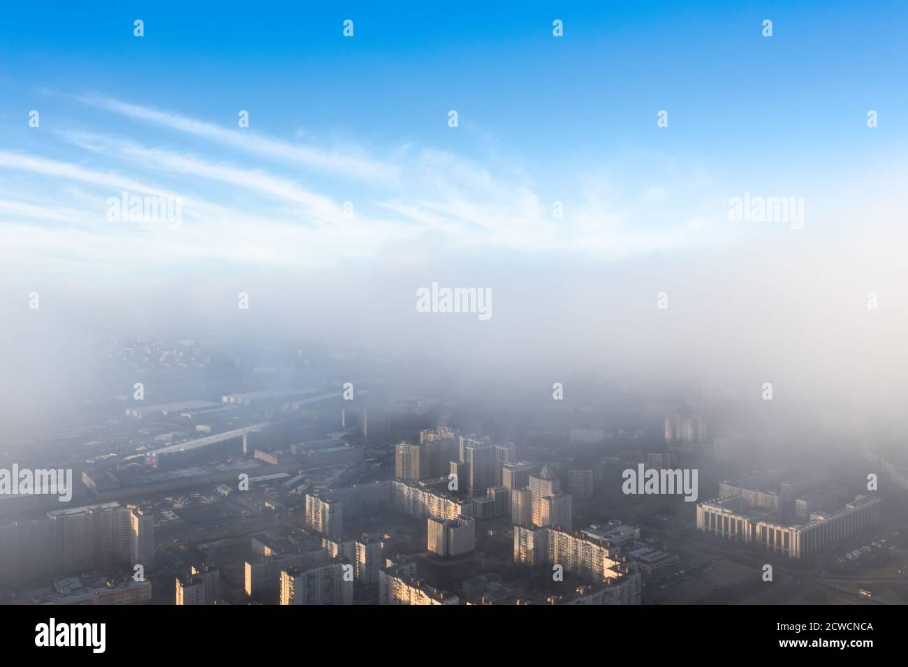 The city is under a layer of fog and low clouds, from above there is a clear blue sky Stock Photo