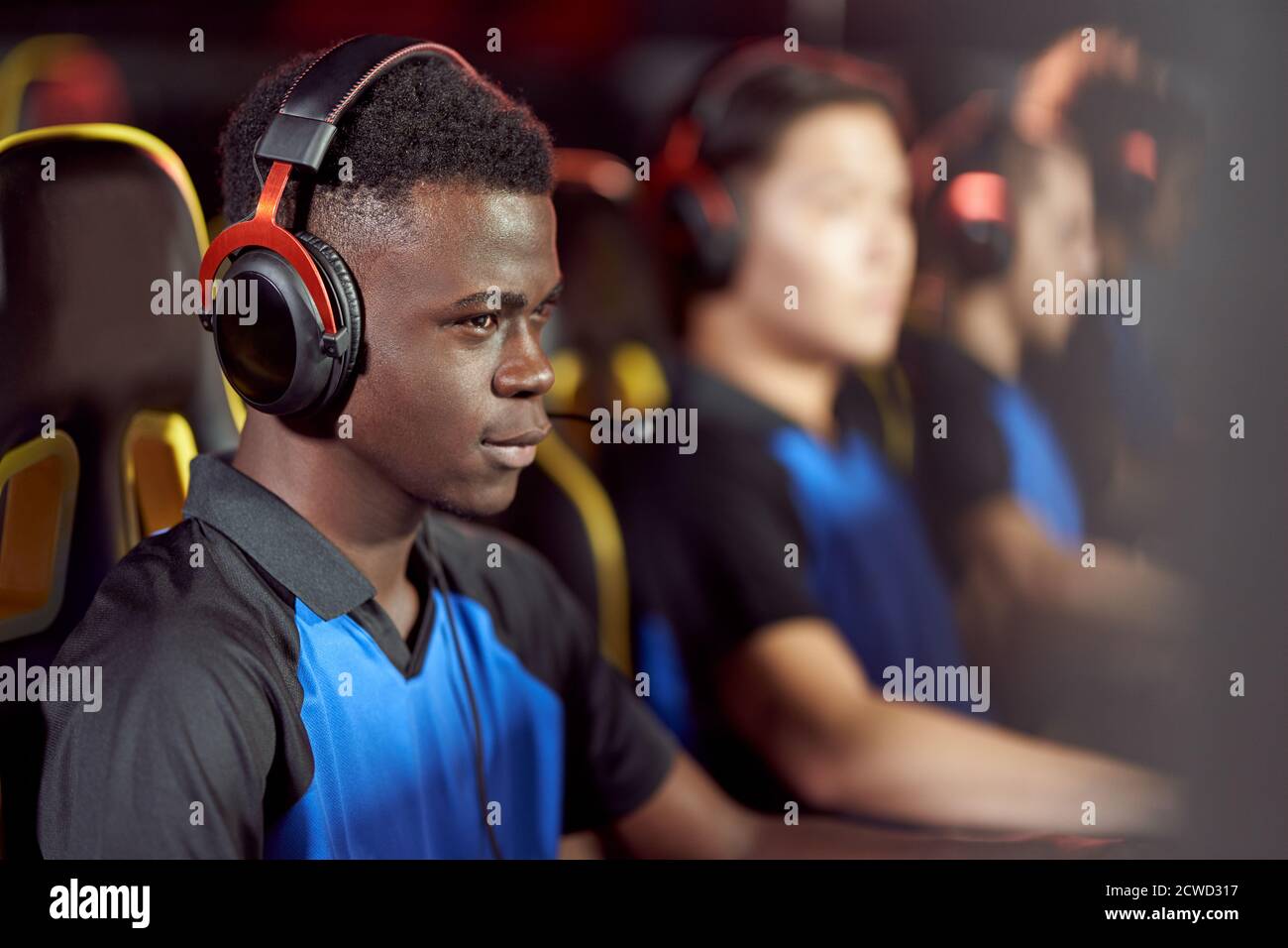 Competition. Side view of african male cybersport male gamer wearing headphones playing video games, participating in eSport tournament while sitting in gaming club or internet cafe Stock Photo