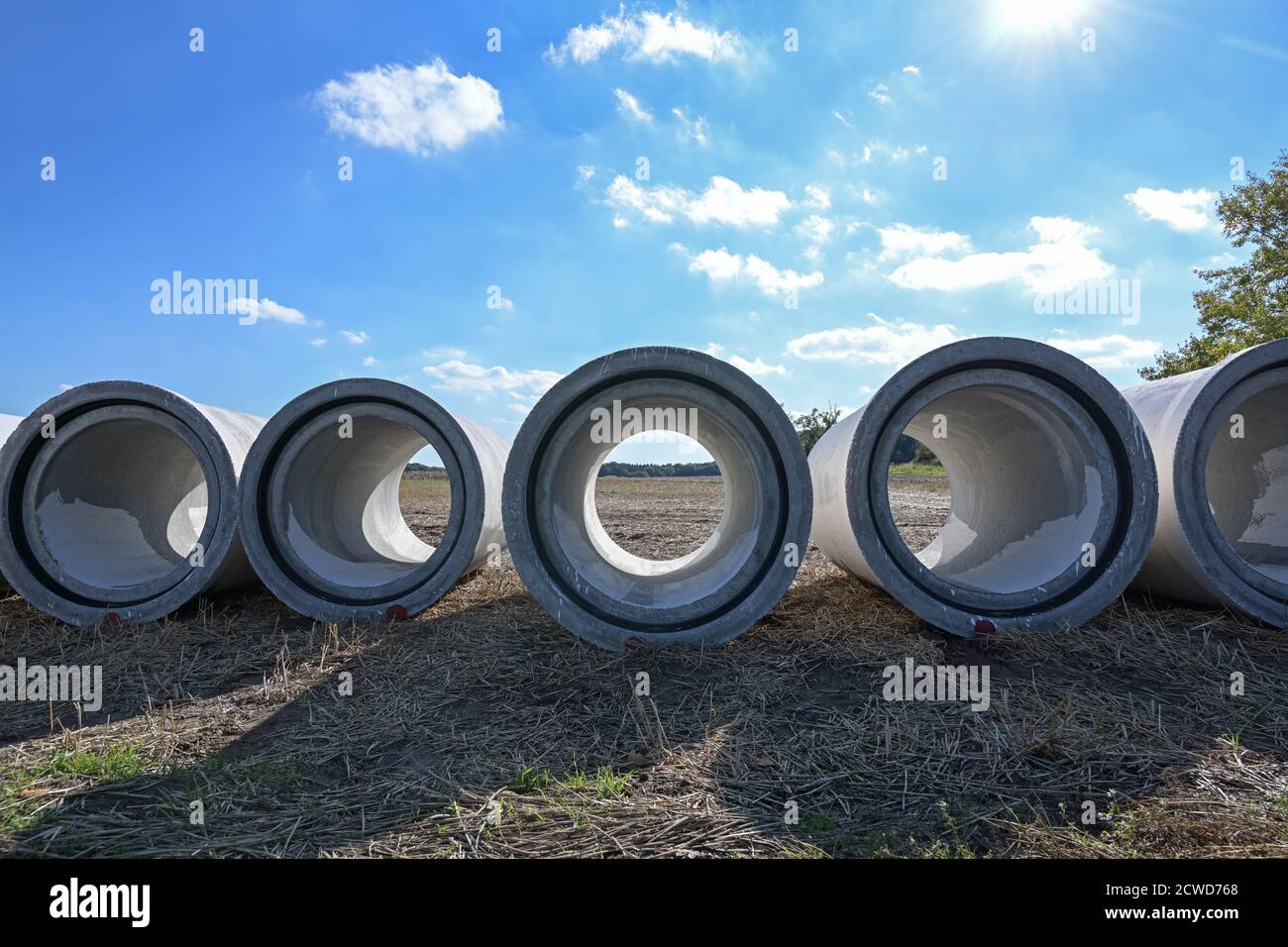 View through concrete water pipes lying side by side on a construction site on a field for a drainage sewage system against flooding, copy space, sele Stock Photo
