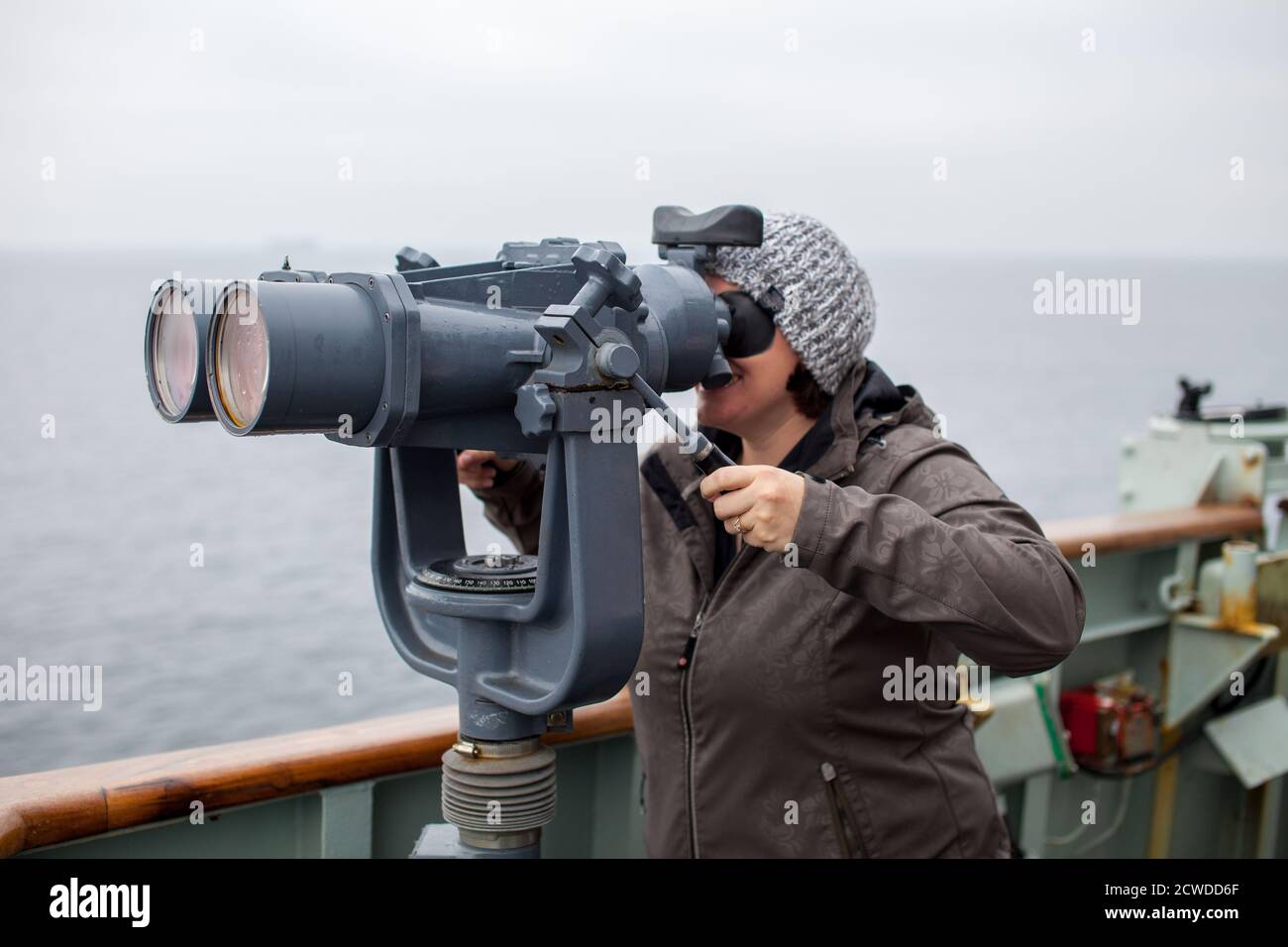 A young woman looks out through ship binoculars out into the open ocean at the Canadian Forces Base in Esquimalt, British Columbia, Canada Stock Photo