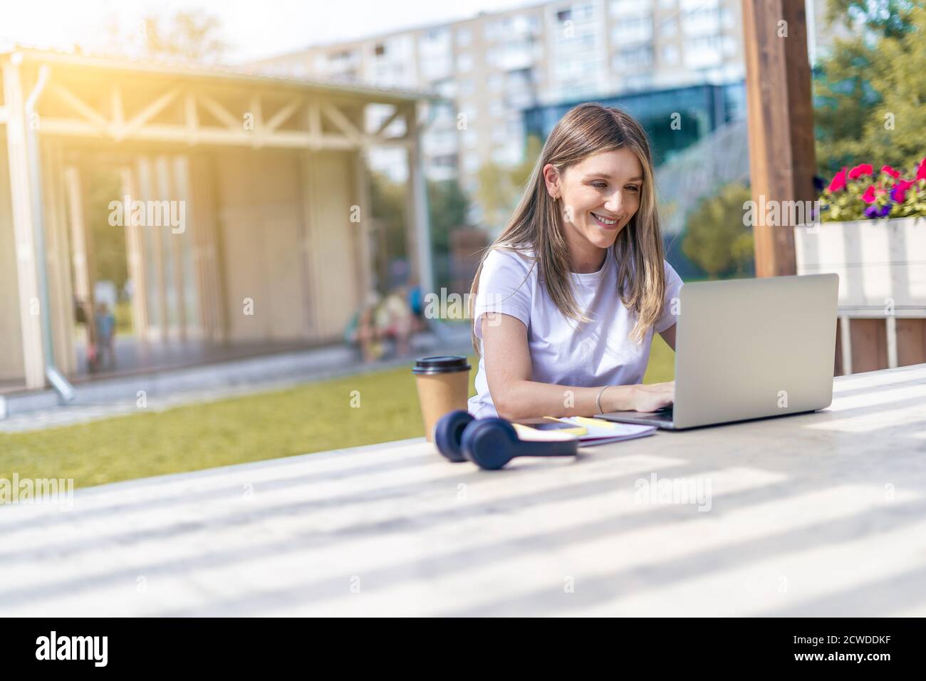 Woman with headphones having a video call with laptop outside in park ...
