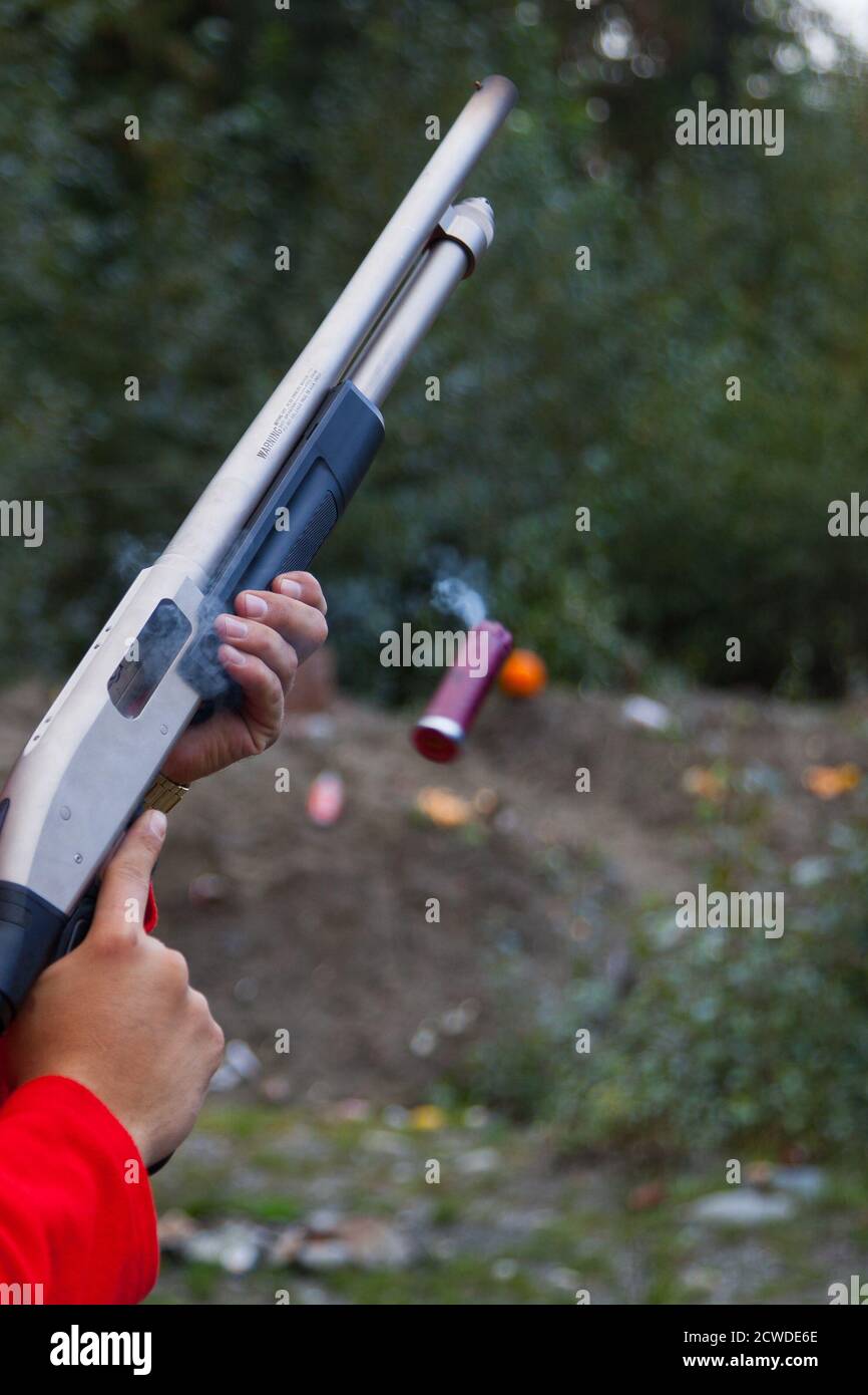 Close up of man holding a shotgun while ejecting the shell from the magazine. The shell is still hot and you can see it smoking as it flies out Stock Photo