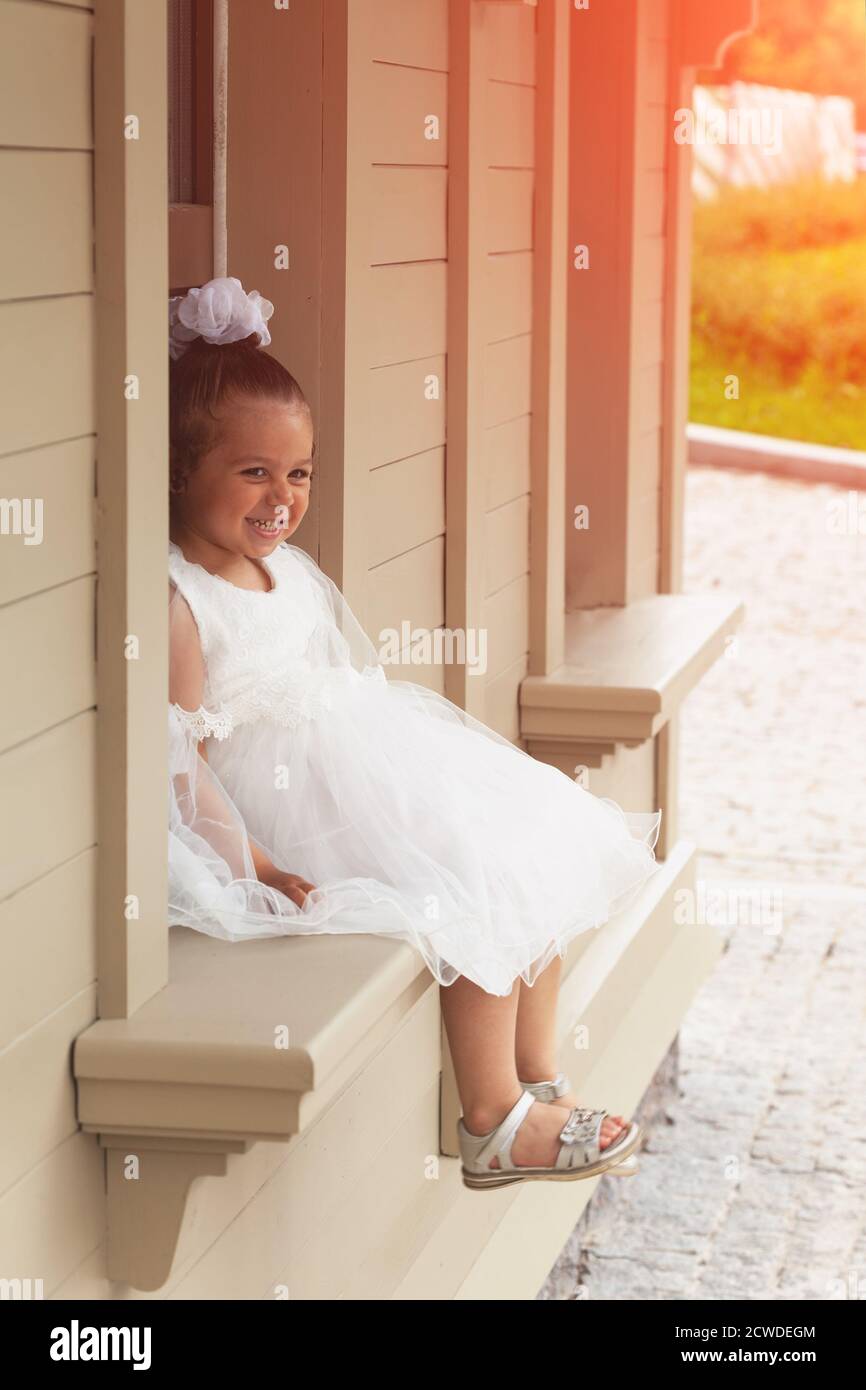 A little girl in a white dress of the bride sits on a windowsill Stock ...