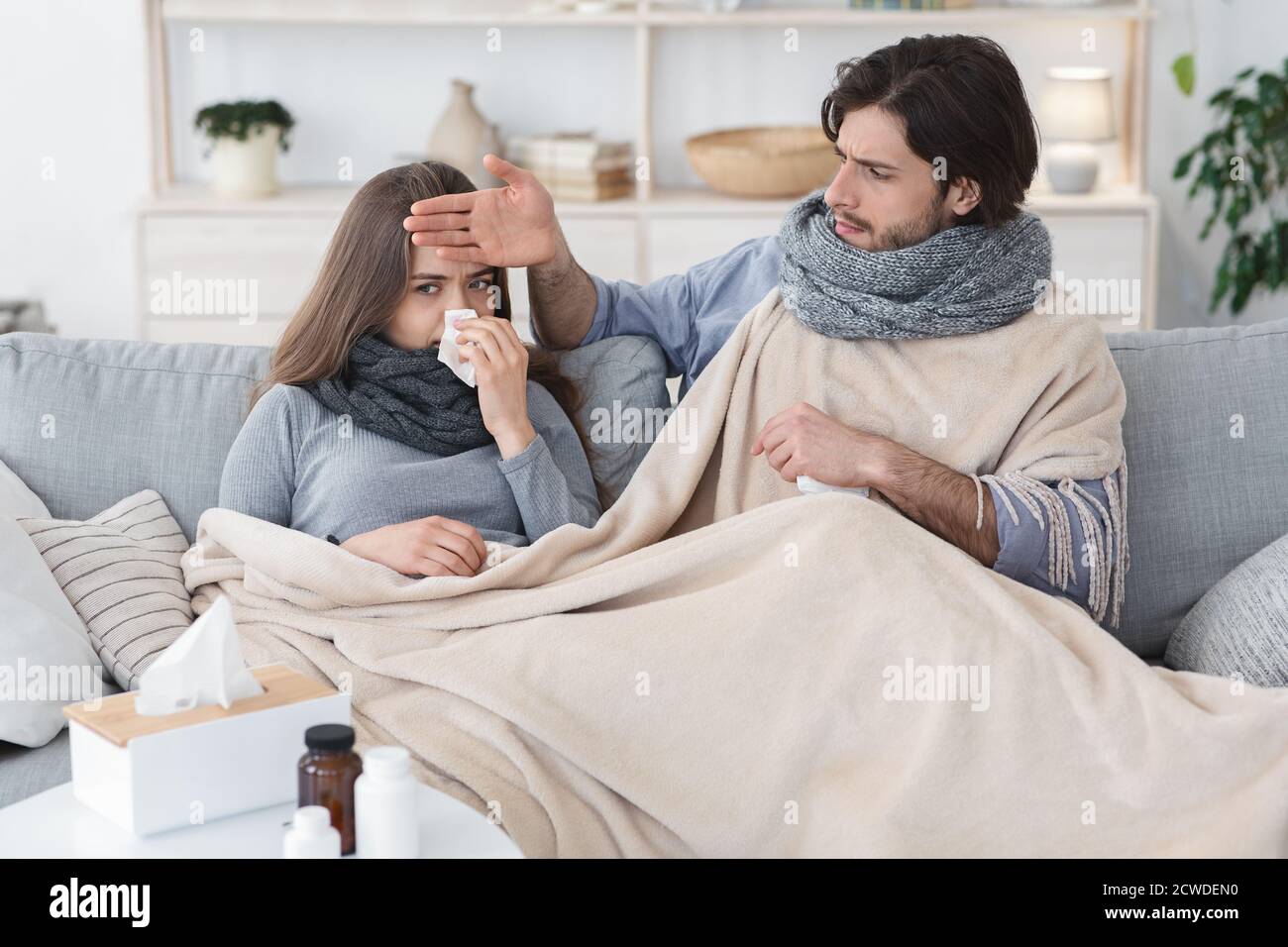 Sick couple covered in blanket sitting on couch, having fever Stock Photo