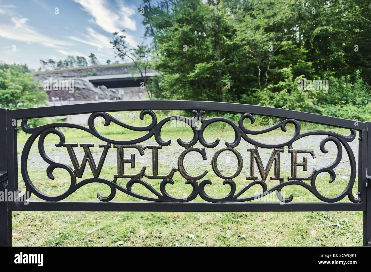 Welcome metal sign on a seat. Trees and bridge in the background Stock Photo