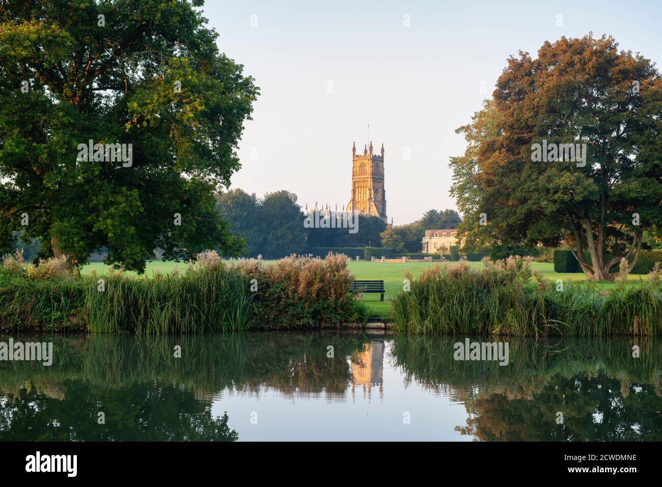 The Church of St. John the Baptist from the abbey grounds reflecting in the abbey lake at sunrise. Cirencester, Cotswolds, Gloucestershire, England Stock Photo