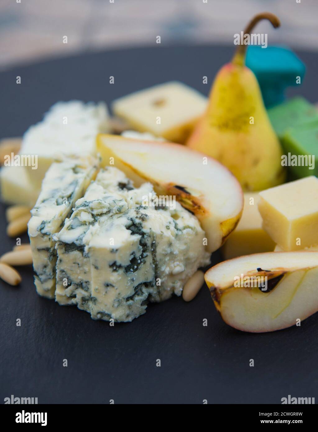 Pieces of various cheeses, ripe pears and pine nuts. Dairy product on the black plate Stock Photo