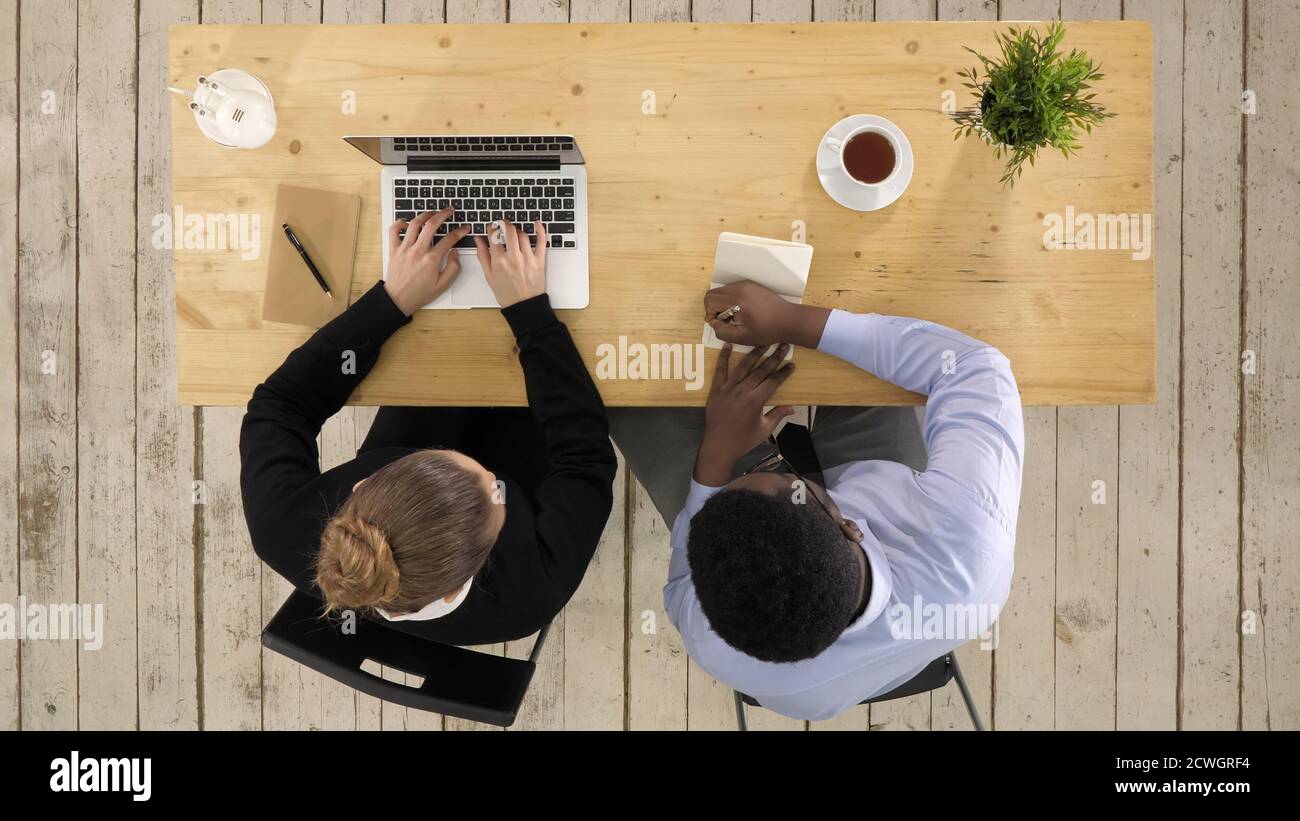Two colleagues discussing data on laptop putting down notes Stock Photo