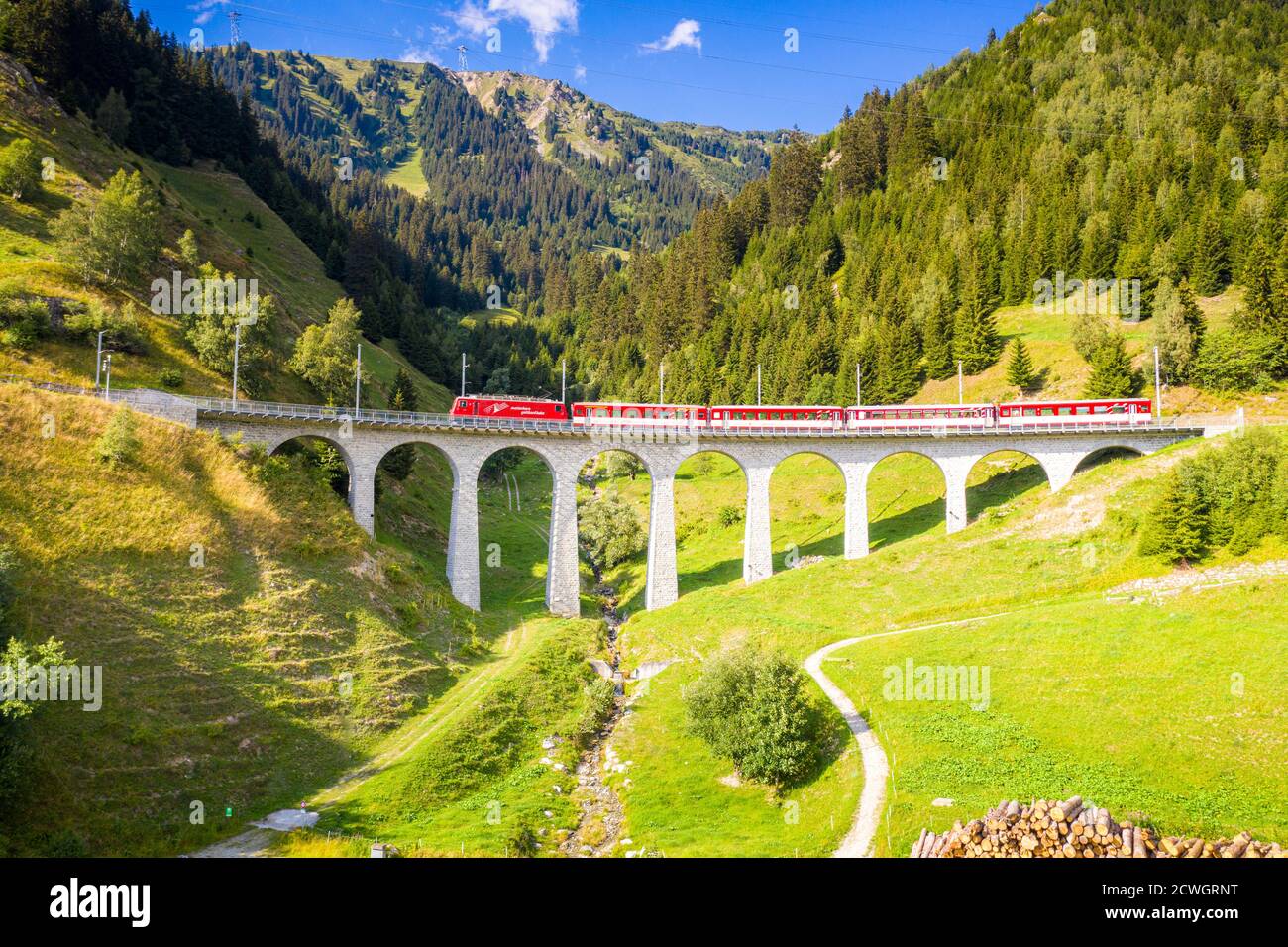 Bright sun over Glacier Express train traveling on Tujetsch viaduct in summer, Sedrun, Graubunden canton, Switzerland Stock Photo