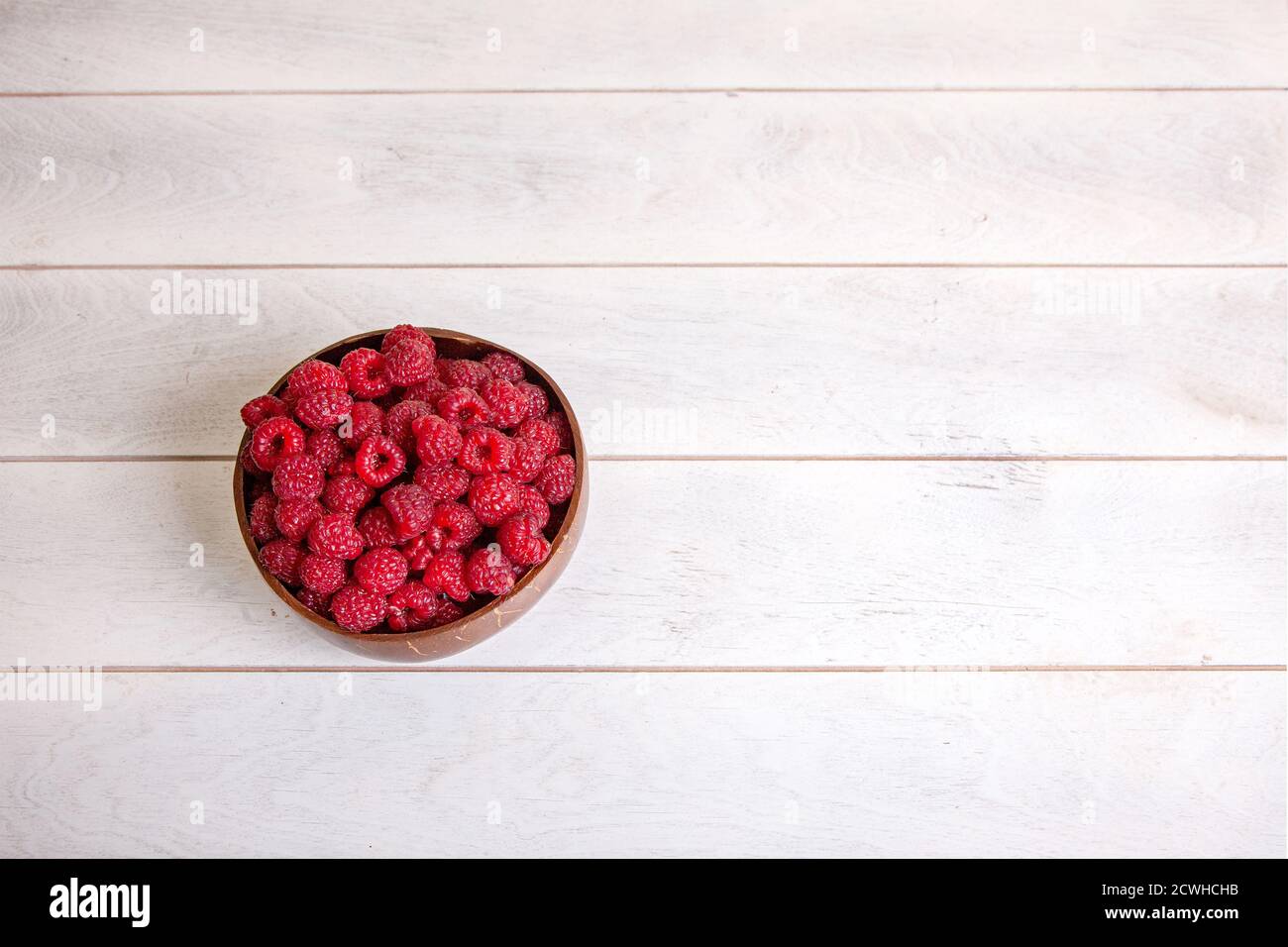 Raspberries in coconut shell bowl on white wooden background, top view ...
