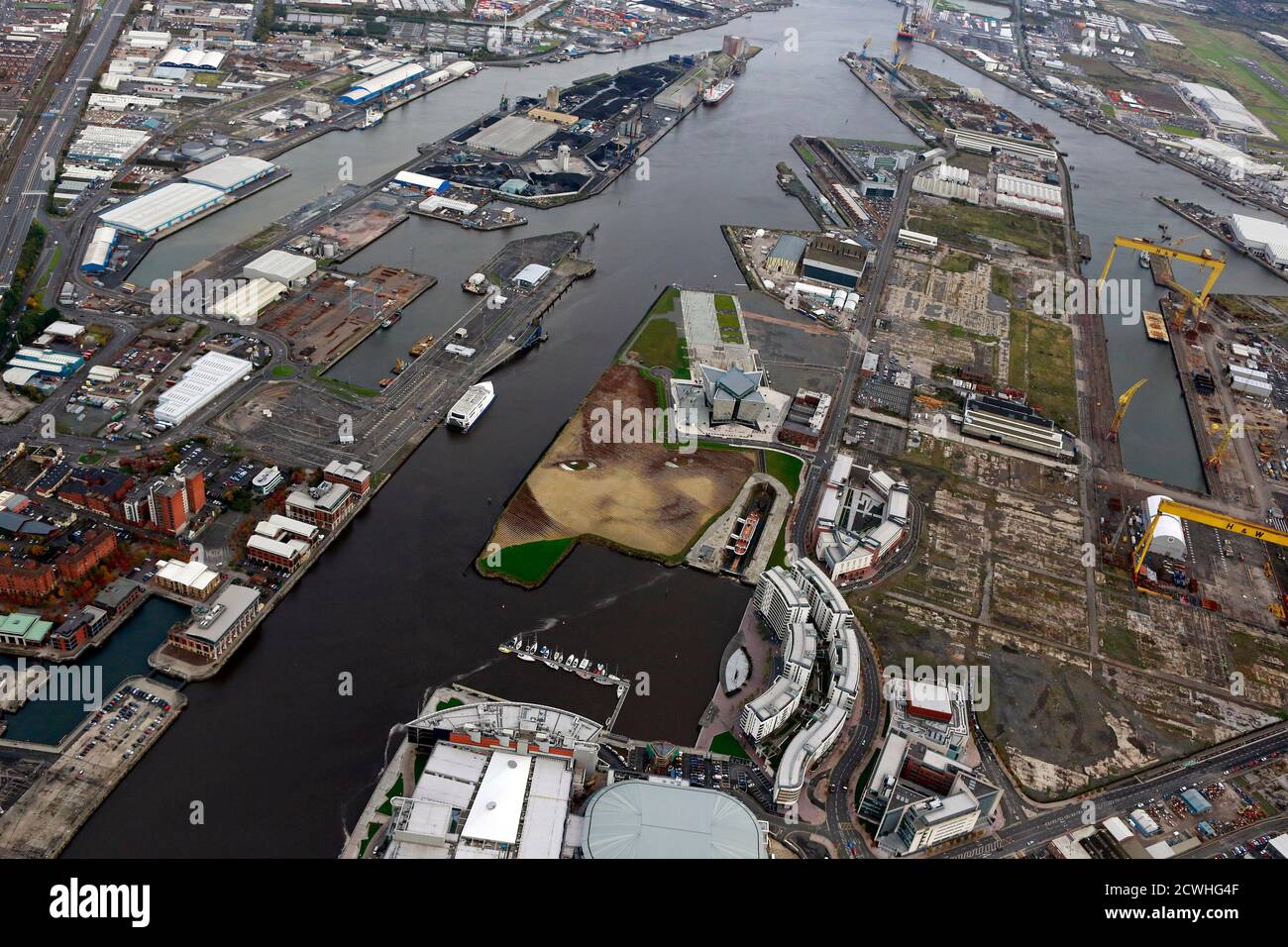 A piece of land art entitled 'Wish' showing the face of an anonymous six-year-old local Belfast girl is seen in this aerial view of the Titanic quarter in Belfast October 23, 2013. The artwork by Cuban-American artist Jorge Rodriguez-Gerada spans 11 acres, is made up from 2,000 tonnes of sand, 2,000 tonnes of soil and some 30,000 wooden pegs. It will remain on view until December 2013.  REUTERS/Cathal McNaughton (NORTHERN IRELAND - Tags: ENTERTAINMENT SOCIETY ENVIRONMENT) Stock Photo
