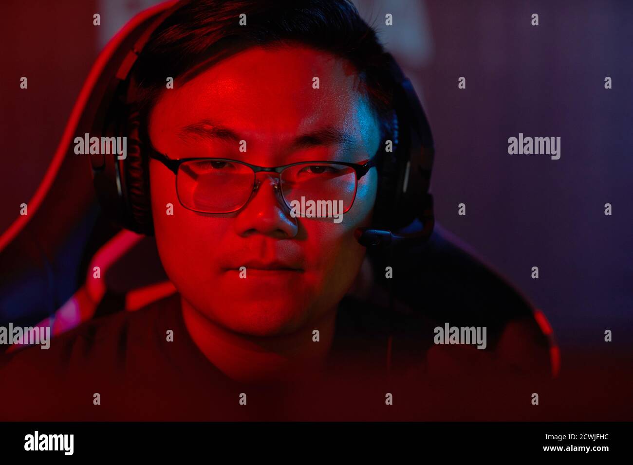 Close-up of Asian developer in eyeglasses and in headphones looking at ...