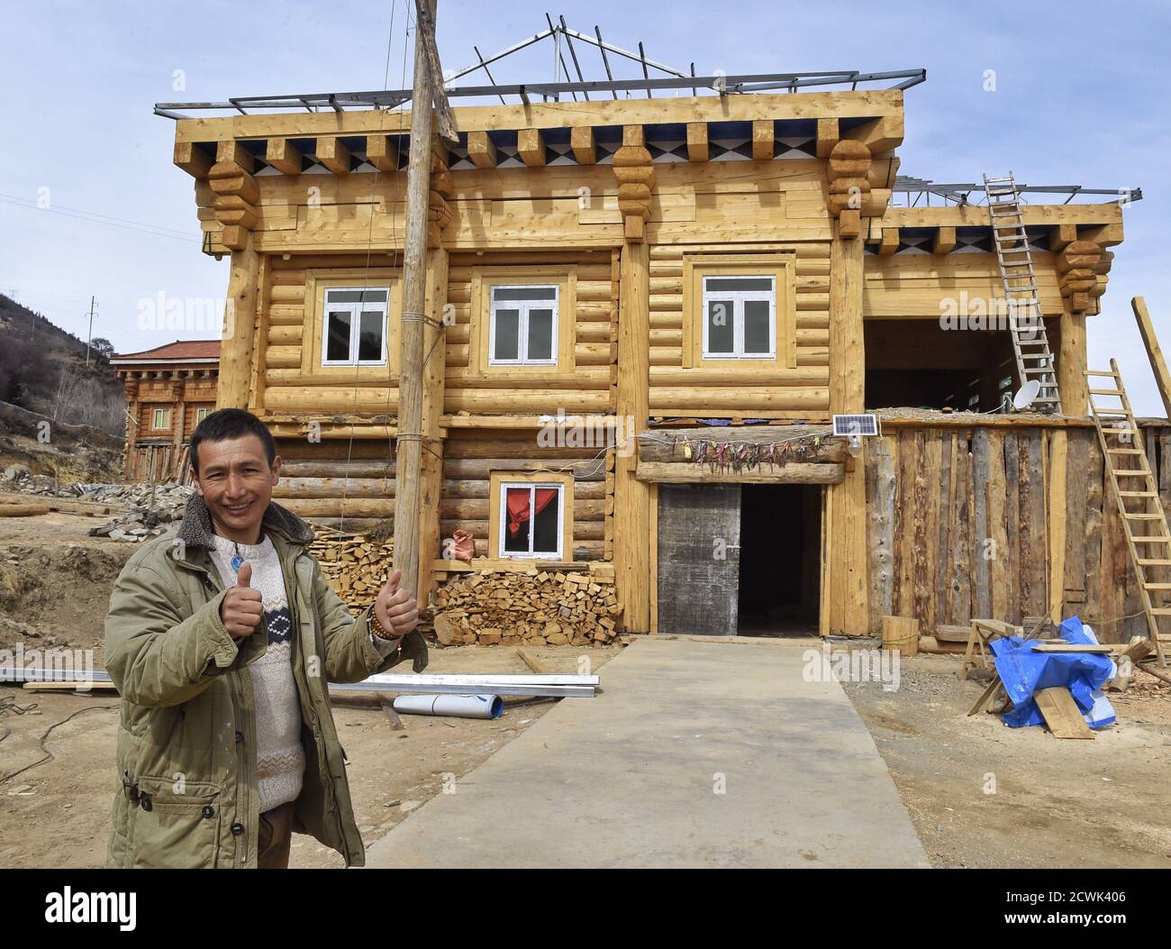 Chengdu, China's Sichuan Province. 11th Mar, 2017. A once poverty-stricken villager poses for a photo with his new house under construction in Geka Village of Mazi Town, Dawu County of Tibetan Autonomous Prefecture of Garze, southwest China's Sichuan Province, March 11, 2017. Credit: Liu Kun/Xinhua/Alamy Live News Stock Photo