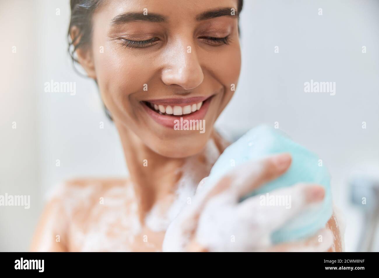 Cheerful young woman washing body with bath loofah Stock Photo