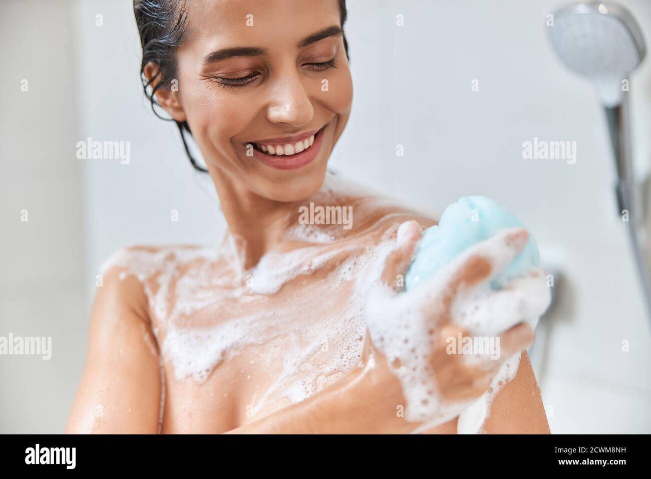 Cheerful young woman using exfoliating loofah while taking shower Stock