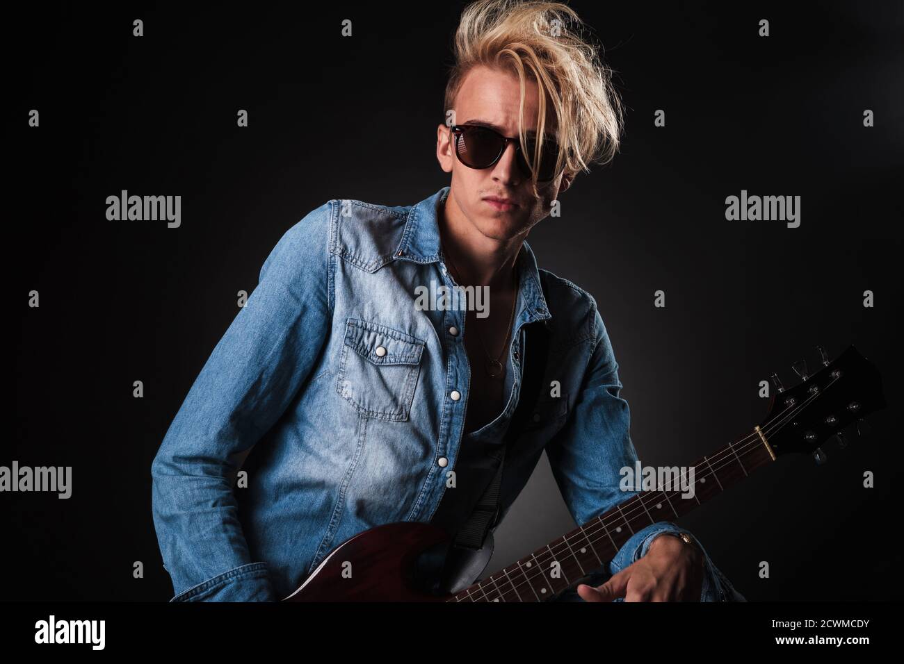 cool young guitarist wearing sunglasses , studio picture on black