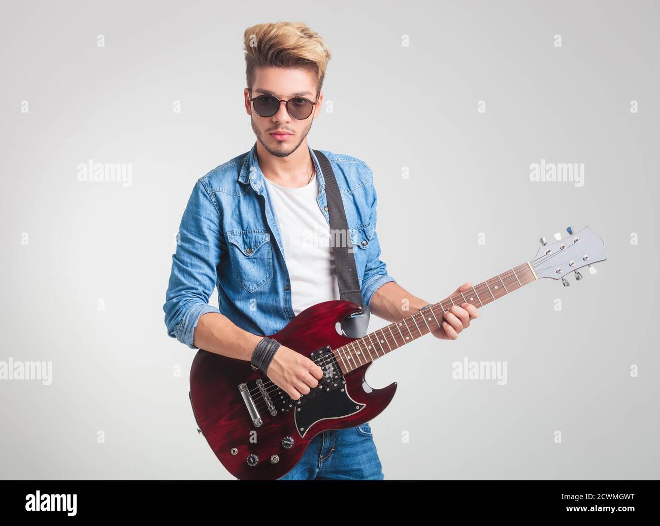 cool blonde guy playing electric guitar while posing for the camera in studio background Stock Photo