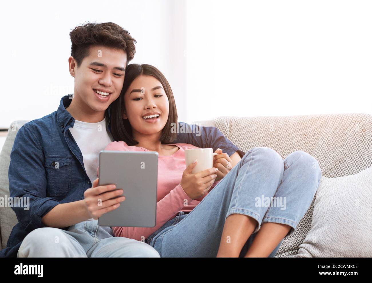 Happy Chinese Couple Using Digital Tablet Relaxing At Home Stock Photo