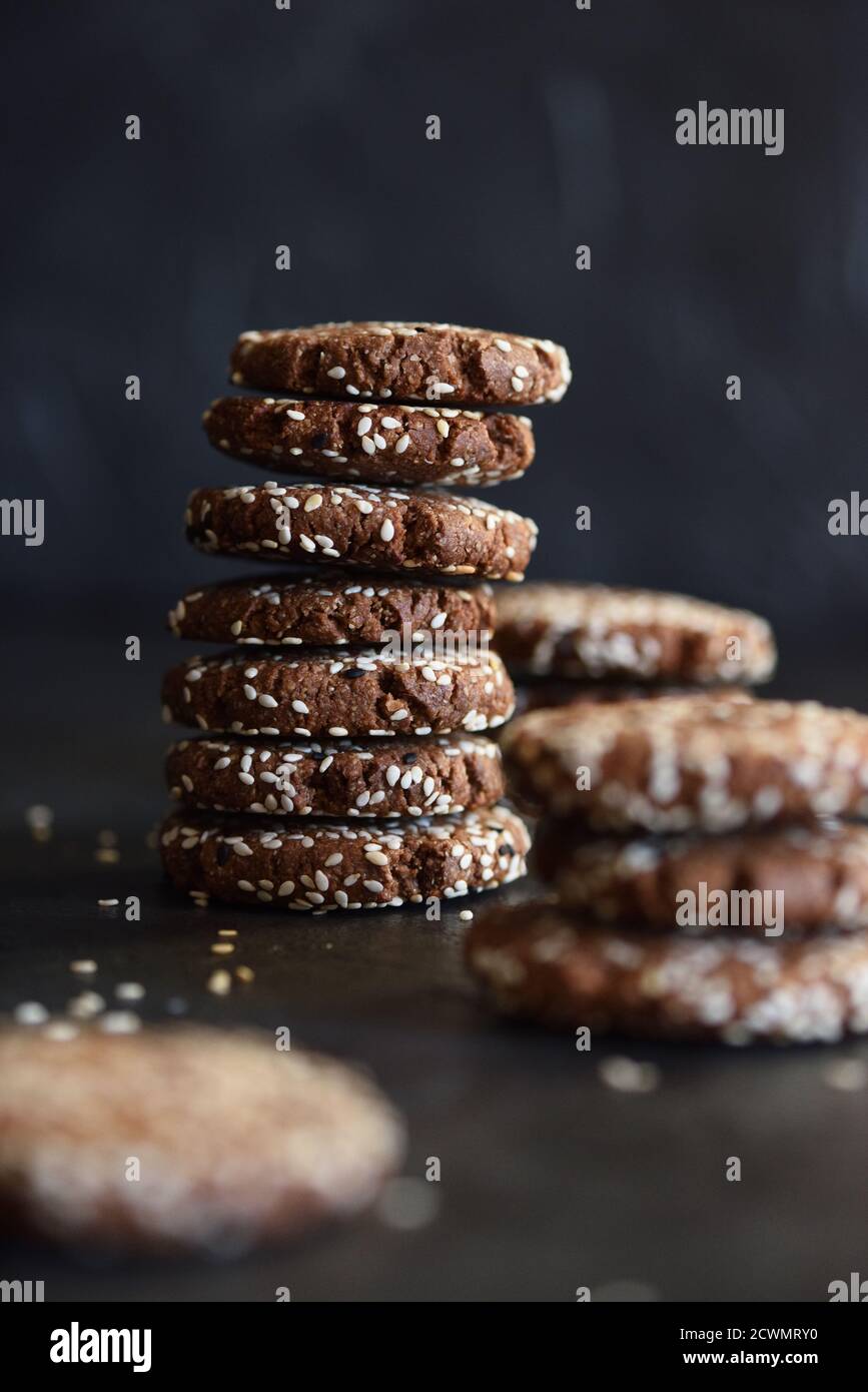 Homemade vegan gluten free chocolate cookies with sesam seeds in pile on black background side view copy space Stock Photo
