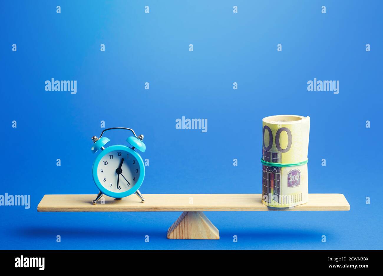 Blue alarm clock and a bundle of euro on scales. Fair hourly wages. Profitability and return on investment. Rental. Balance between life and career. T Stock Photo