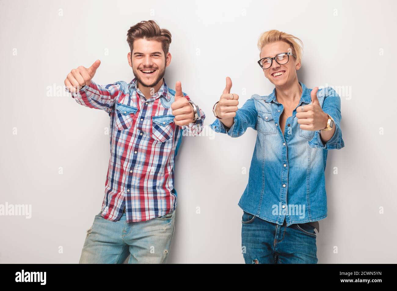two happy young casual men making the ok thumbs up hand gesture in ...