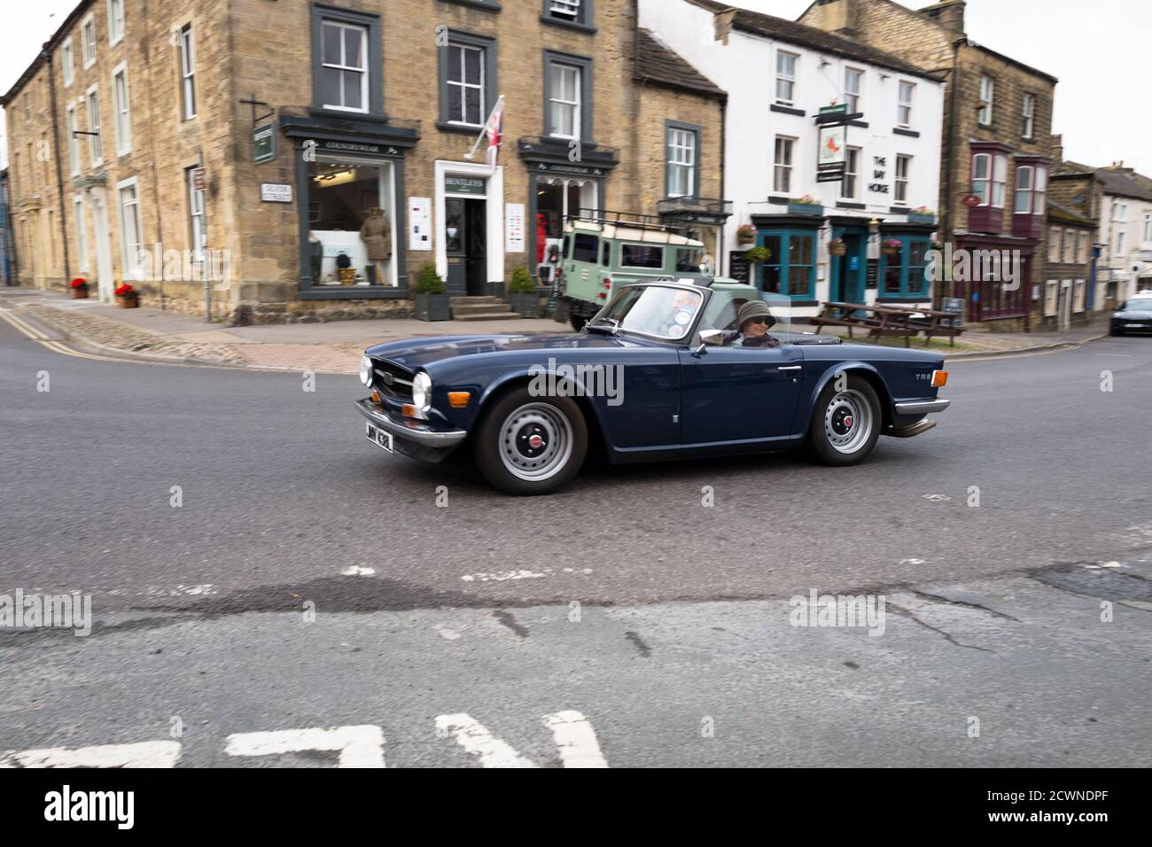 Couple in a open top Triumph TR6 sports car drive through the Yorkshire Dales village of Masham, Engalnd. Stock Photo