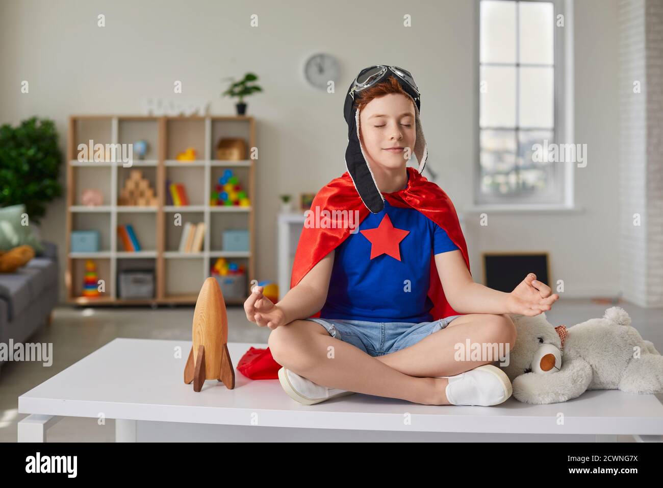 Funny little boy sitting on the table in the lotus position in the nursery. Stock Photo