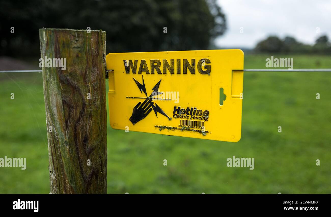 Electric fence yellow warning sign attached to a electrified cattle wired fence. Stock Photo