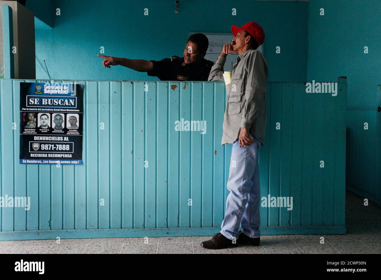 A citizen speaks to a policeman at the reception next to a wanted poster at Tegucigalpa police station October 15, 2010. From (L-R) Angel Martinez, 23, know as 'Crazy Horse'(fugitive); Mario Guevara (temporarily released for lack of evidence), Marcos Alvarez, 35, know as 'Unicorn' (captured on 22 September) and Terry Thompson (fugitive) alleged perpetrators for the murder of journalist David Meza Montecinos on March 11, according to police spokesman Leonel Sauceda in Tegucigalpa. Nine journalists have been killed and one radio announcer in Honduras during 2010, according to Honduras police. Th Stock Photo