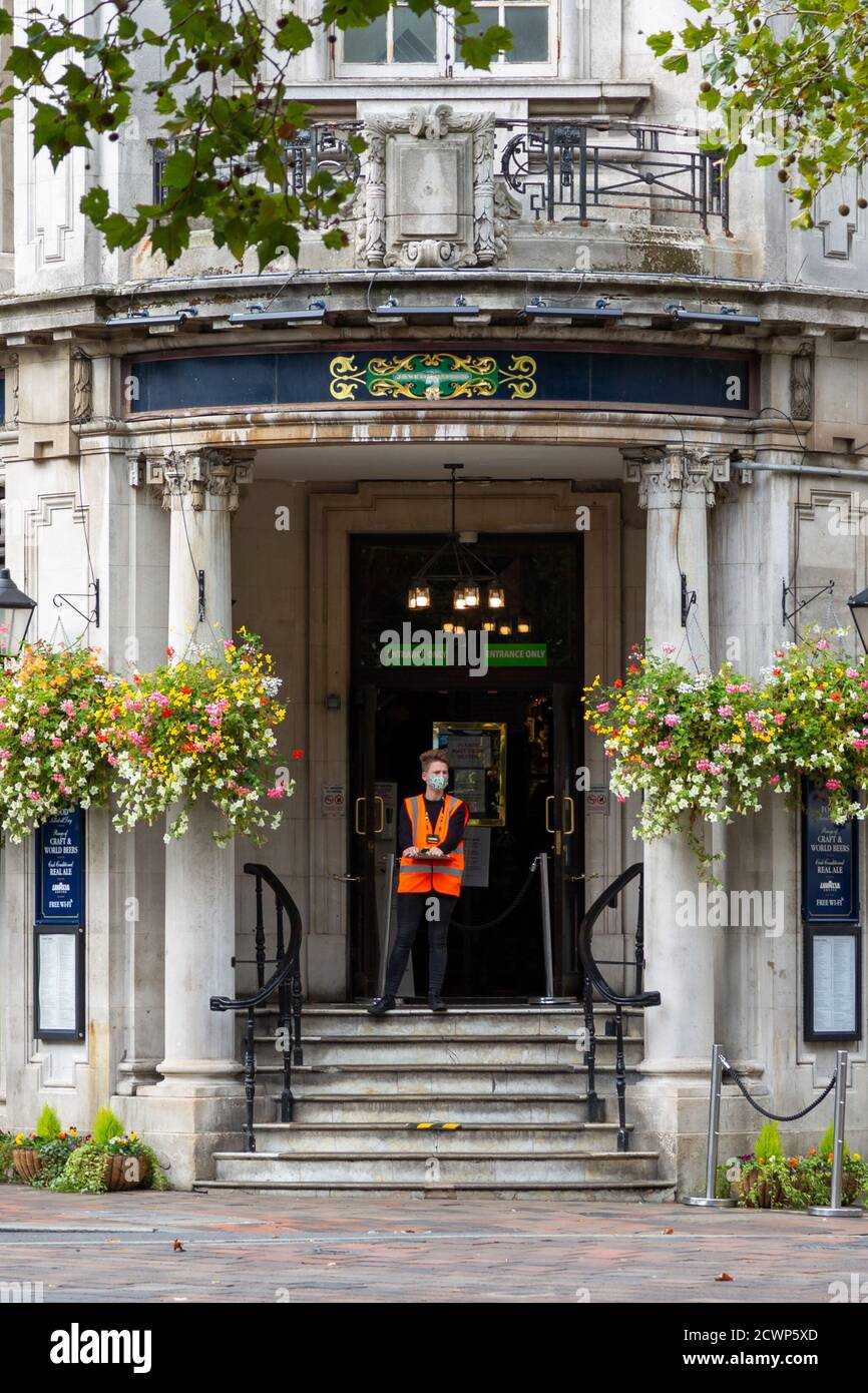 A doorman wearing a face mask at the entrance of a pub waiting to sign people in using track and trace during the coronavirus pandemic Stock Photo